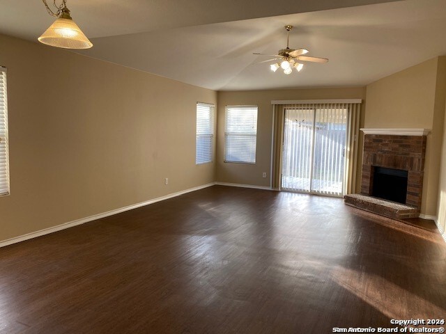 unfurnished living room featuring a fireplace, vaulted ceiling, ceiling fan, and dark wood-type flooring