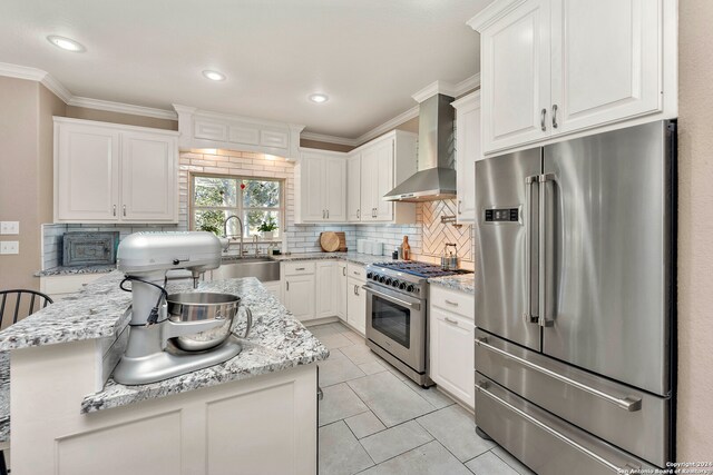 kitchen with decorative backsplash, light stone counters, premium appliances, wall chimney range hood, and white cabinetry