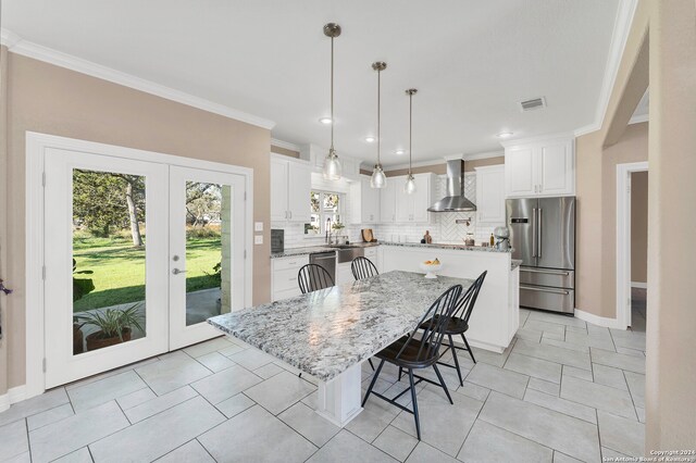 kitchen with a center island, white cabinets, wall chimney range hood, and appliances with stainless steel finishes