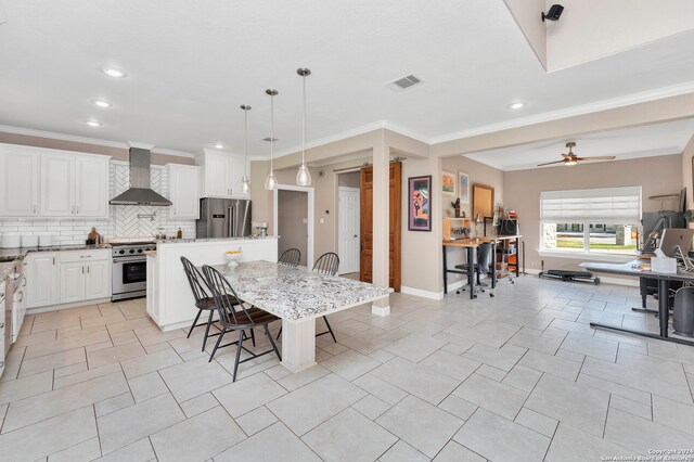 kitchen featuring appliances with stainless steel finishes, ceiling fan, wall chimney range hood, pendant lighting, and a breakfast bar area