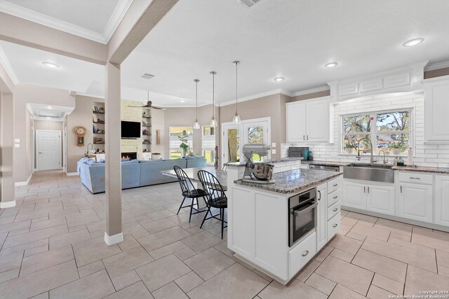 kitchen with white cabinetry, a center island, stainless steel oven, backsplash, and stone countertops