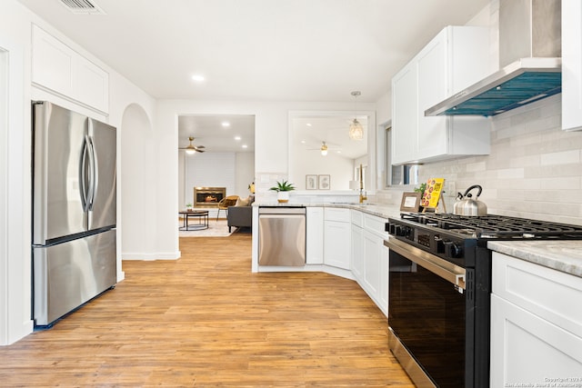 kitchen with white cabinetry, light hardwood / wood-style flooring, wall chimney exhaust hood, and appliances with stainless steel finishes