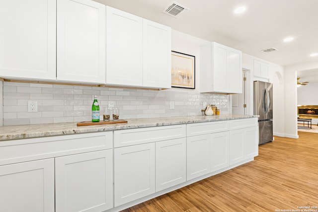 kitchen featuring white cabinetry, light stone counters, backsplash, stainless steel fridge, and light hardwood / wood-style floors