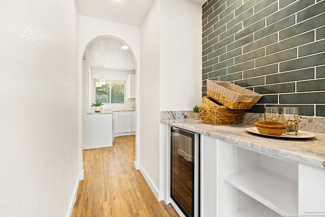 bar with white cabinets, light hardwood / wood-style flooring, beverage cooler, and light stone counters