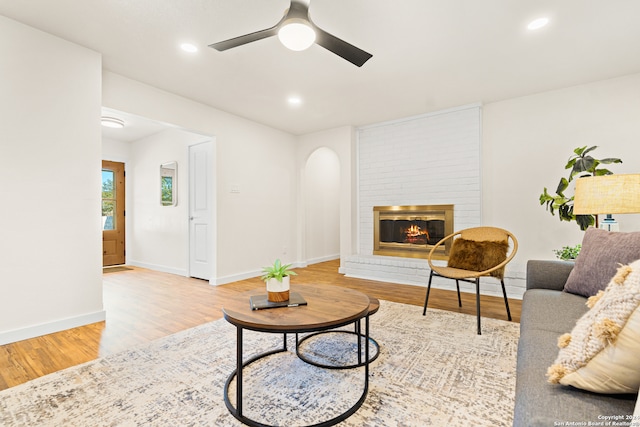 living room featuring light wood-type flooring, a brick fireplace, and ceiling fan