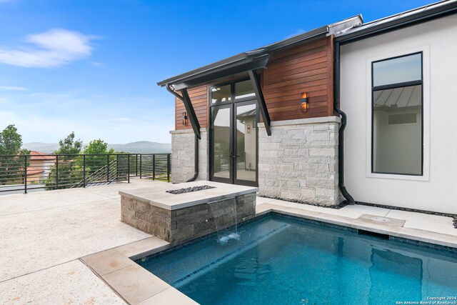 view of pool with pool water feature, a mountain view, a fire pit, and a patio