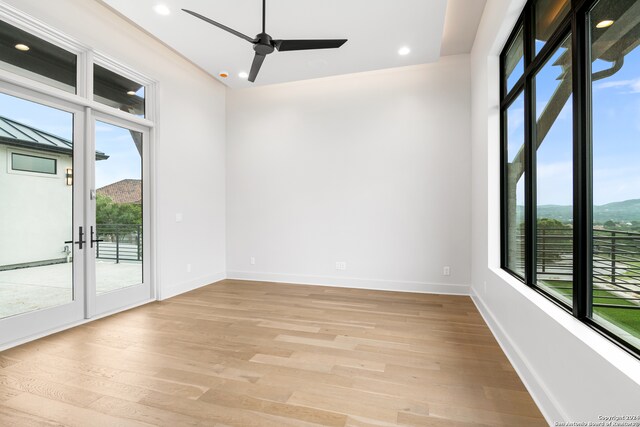 empty room featuring a mountain view, a healthy amount of sunlight, ceiling fan, and light hardwood / wood-style flooring