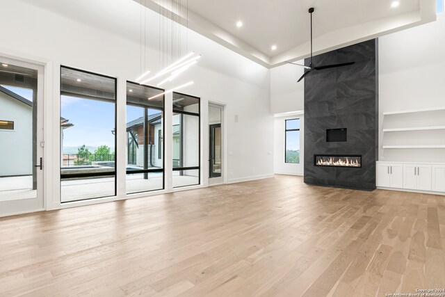 unfurnished living room featuring built in shelves, ceiling fan, a high ceiling, a fireplace, and light wood-type flooring