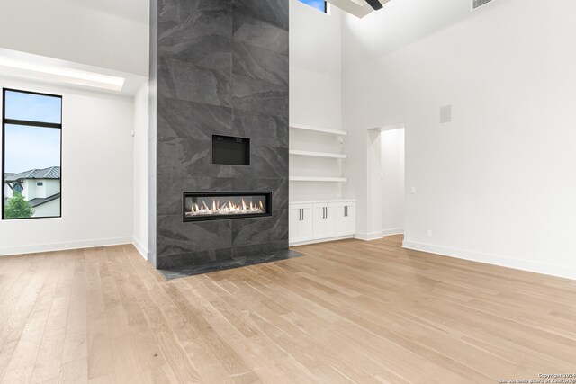 unfurnished living room featuring built in shelves, a tiled fireplace, and light hardwood / wood-style flooring