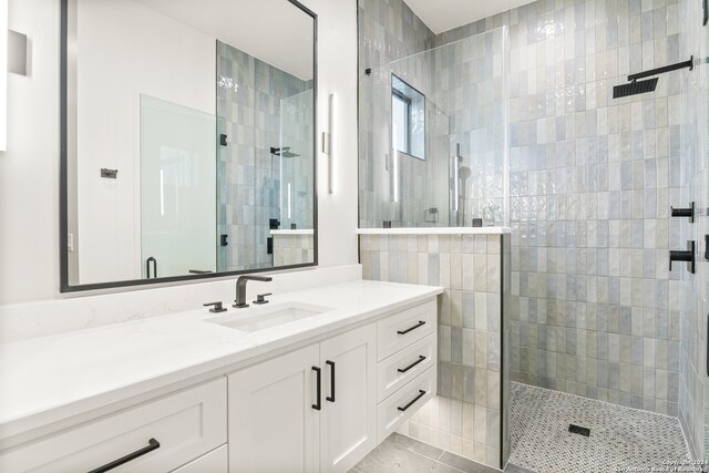 bathroom with tile patterned flooring, a tile shower, and vanity