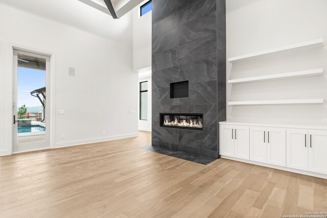 unfurnished living room with built in shelves, a fireplace, a towering ceiling, and light hardwood / wood-style floors