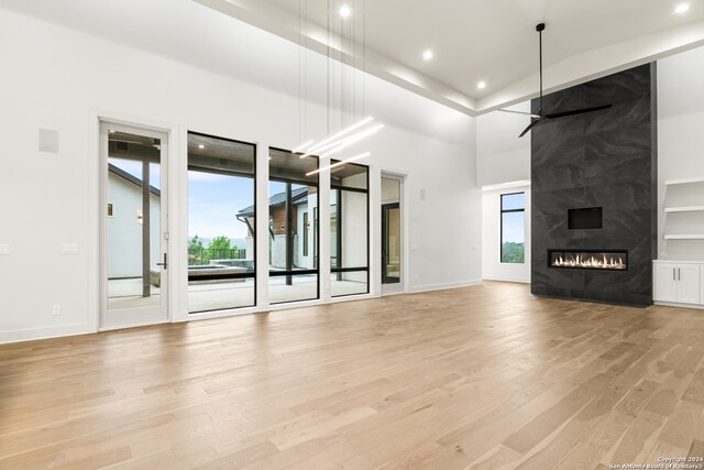 unfurnished living room featuring ceiling fan, a fireplace, a towering ceiling, and light hardwood / wood-style flooring