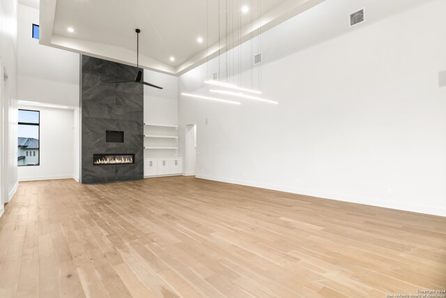 unfurnished living room featuring a tiled fireplace, ceiling fan, light hardwood / wood-style flooring, and a towering ceiling