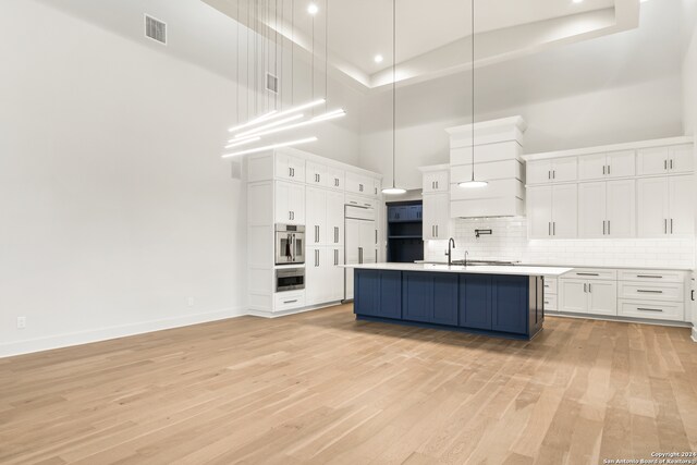 kitchen with white cabinets, light hardwood / wood-style flooring, a towering ceiling, and decorative light fixtures