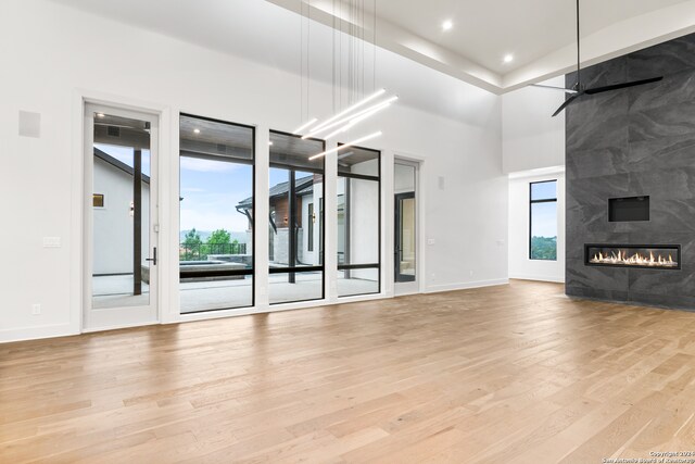 unfurnished living room with a tiled fireplace, light hardwood / wood-style flooring, and a high ceiling