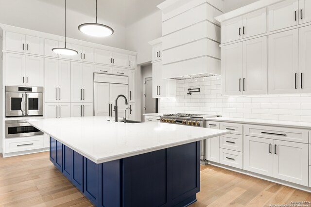 kitchen featuring premium appliances, pendant lighting, light hardwood / wood-style flooring, white cabinets, and an island with sink