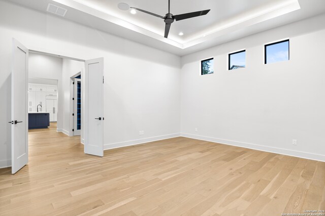 empty room with ceiling fan, light wood-type flooring, and a tray ceiling