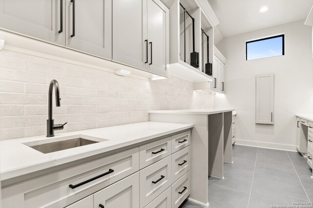 kitchen featuring decorative backsplash, white cabinetry, sink, and light tile patterned floors