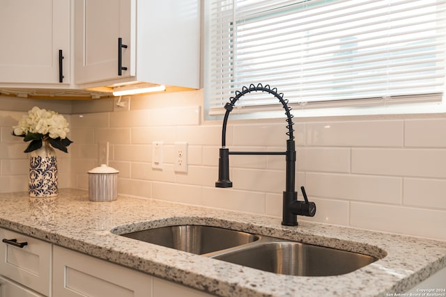 interior details featuring light stone countertops, backsplash, white cabinetry, and sink