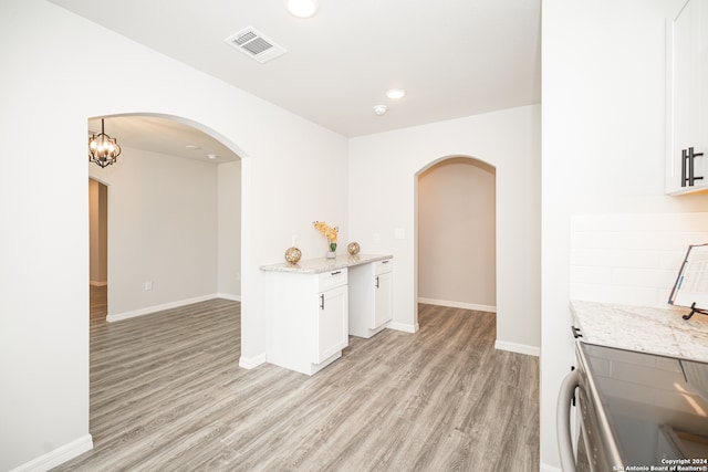 interior space with light stone countertops, pendant lighting, light hardwood / wood-style flooring, a notable chandelier, and white cabinetry