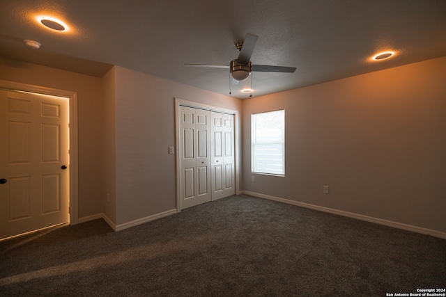 unfurnished bedroom featuring dark colored carpet, ceiling fan, a textured ceiling, and a closet