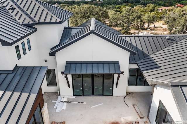 rear view of house featuring metal roof, a standing seam roof, and stucco siding