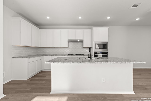 kitchen with appliances with stainless steel finishes, light stone counters, a kitchen island with sink, wood-type flooring, and white cabinetry