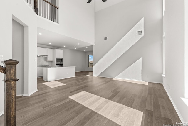 unfurnished living room featuring ceiling fan, hardwood / wood-style floors, and a high ceiling