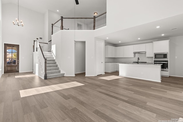 unfurnished living room with a notable chandelier, light wood-type flooring, sink, and high vaulted ceiling