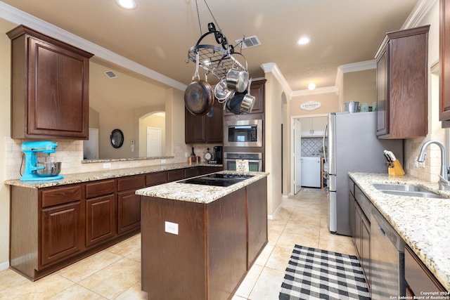 kitchen with sink, light tile patterned floors, ornamental molding, appliances with stainless steel finishes, and a kitchen island