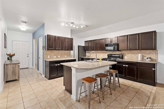 kitchen featuring sink, stainless steel fridge, a kitchen breakfast bar, light stone counters, and a center island with sink