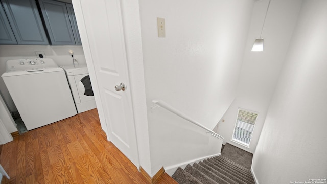 laundry area featuring washing machine and dryer, light hardwood / wood-style flooring, and cabinets