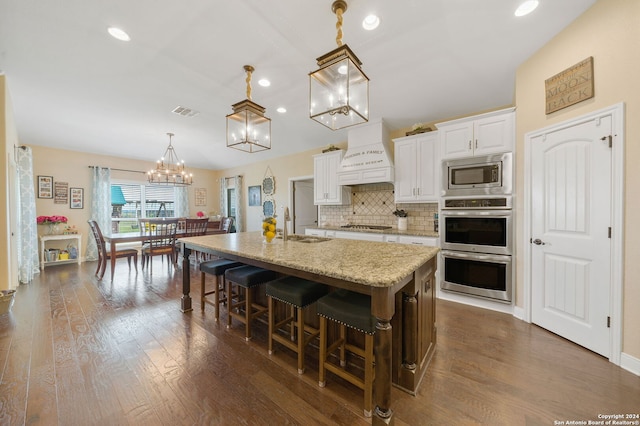 kitchen with premium range hood, stainless steel appliances, a kitchen island with sink, pendant lighting, and white cabinetry