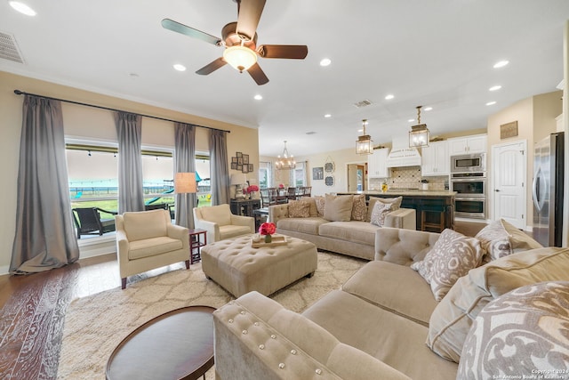 living room featuring ceiling fan with notable chandelier, light hardwood / wood-style floors, and ornamental molding