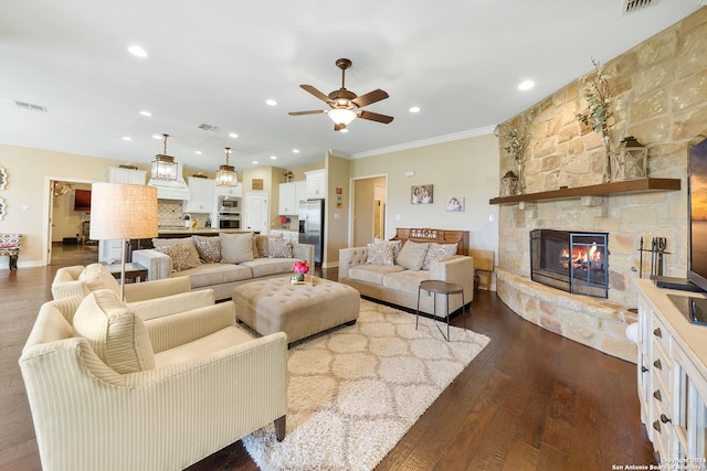 living room featuring hardwood / wood-style flooring, a stone fireplace, ceiling fan, and crown molding