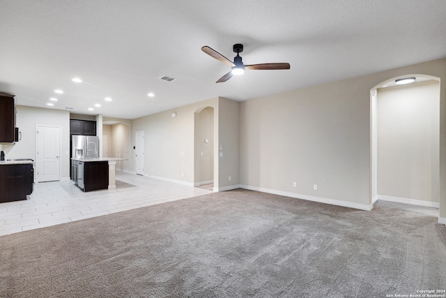 unfurnished living room featuring light carpet, ceiling fan, and a textured ceiling