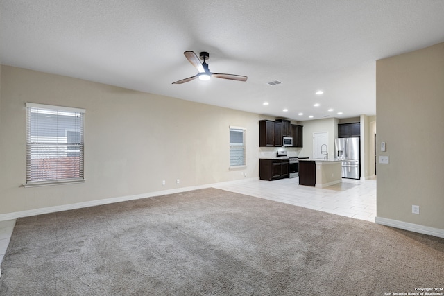 unfurnished living room with a textured ceiling, light colored carpet, ceiling fan, and sink