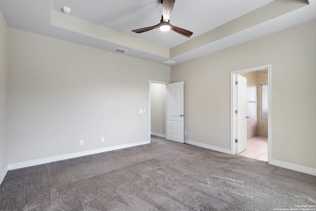 unfurnished bedroom featuring a raised ceiling, ensuite bathroom, ceiling fan, and light carpet