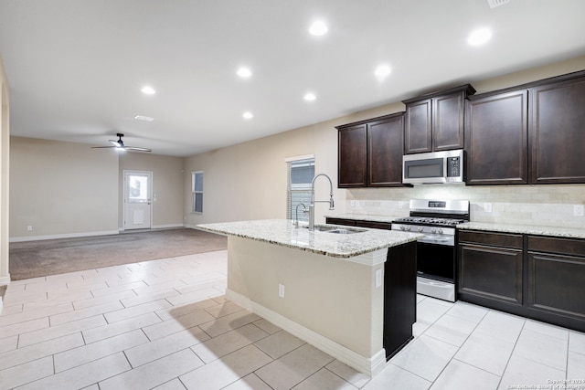 kitchen with light carpet, a center island with sink, sink, ceiling fan, and stainless steel appliances