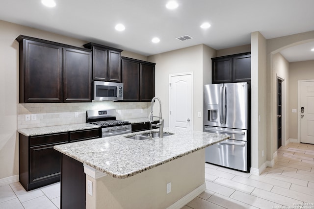 kitchen with sink, light stone counters, an island with sink, decorative backsplash, and appliances with stainless steel finishes