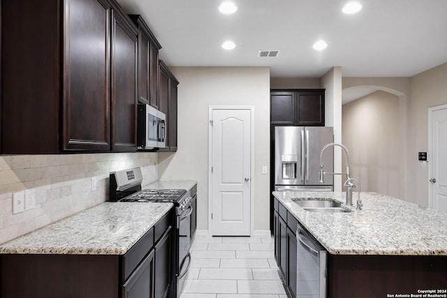 kitchen with decorative backsplash, light stone counters, stainless steel appliances, sink, and a center island with sink