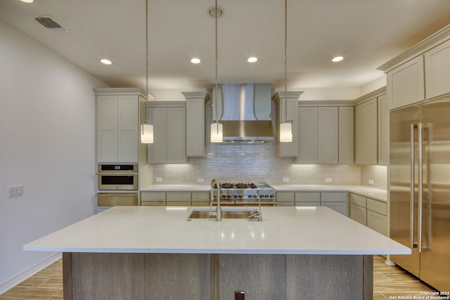 kitchen with a center island with sink, sink, wall chimney exhaust hood, appliances with stainless steel finishes, and light hardwood / wood-style floors