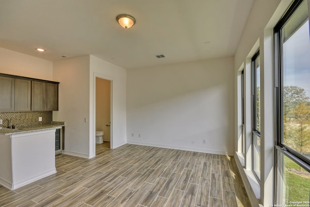 kitchen with light wood-type flooring, tasteful backsplash, light stone counters, dark brown cabinetry, and beverage cooler