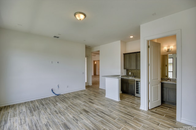 interior space featuring backsplash, wine cooler, light stone countertops, and sink