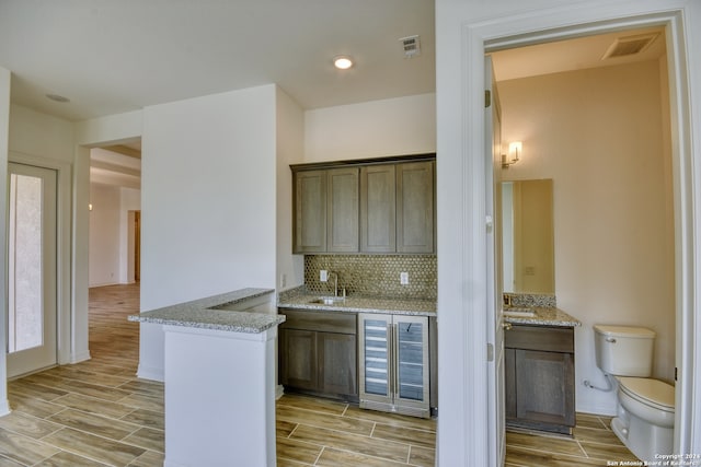 kitchen with light stone counters, light wood-type flooring, backsplash, and beverage cooler