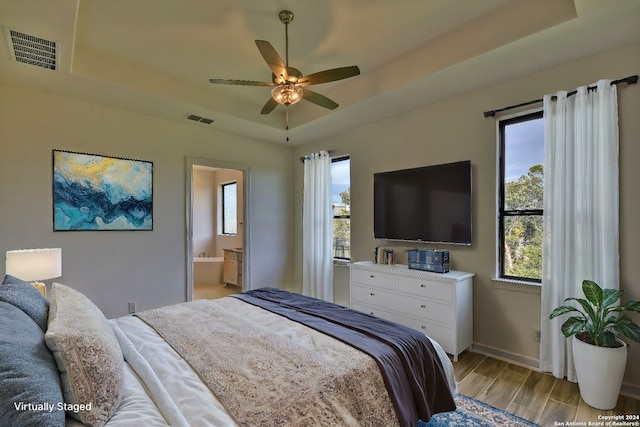 bedroom featuring connected bathroom, a tray ceiling, and multiple windows