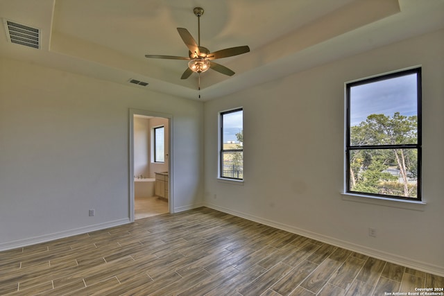 empty room with ceiling fan, wood-type flooring, and a tray ceiling