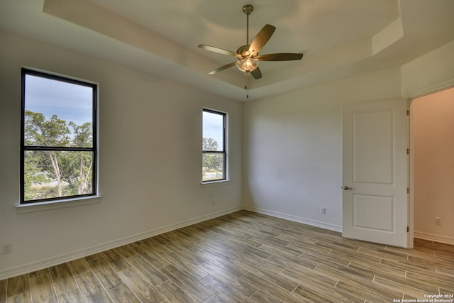 empty room featuring a raised ceiling, ceiling fan, and light hardwood / wood-style floors