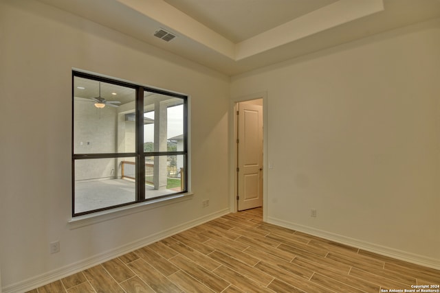 unfurnished room featuring a raised ceiling, ceiling fan, and light wood-type flooring