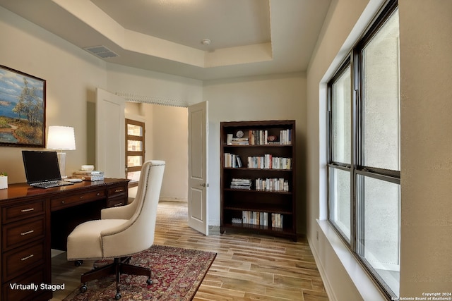 office area with a raised ceiling, light hardwood / wood-style flooring, and a healthy amount of sunlight